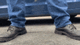 a person wearing blue jeans and black shoes is standing in front of a car