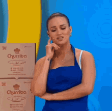 a woman in a blue apron is standing next to a stack of boxes .