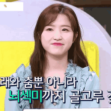 a woman in a blue shirt is smiling in front of a yellow background with foreign writing on it