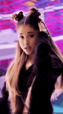 ariana grande is wearing a black fur coat and holding her hair in buns .