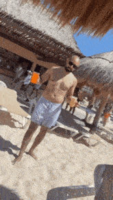 a man without a shirt is standing on the beach holding a drink