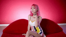 a young woman with pink hair is sitting on a red couch