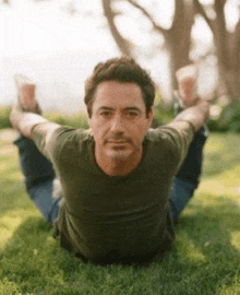 a man in a green shirt is laying on the grass stretching his legs .