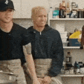 two men standing next to each other in a kitchen with one wearing a hat with a ny logo on it