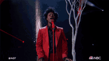 a man in a red suit singing into a microphone with nbc written on the bottom