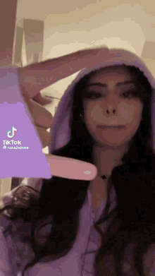 a woman is wearing a purple hoodie and holding a pink object .