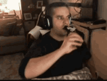 a man wearing headphones is eating a chocolate bar while sitting in a chair in a living room .