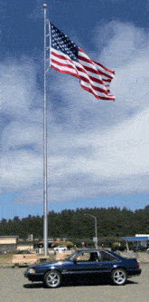 a blue mustang is parked in front of a tall american flag
