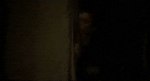 a man is peeking out from behind a wall in a dark room .
