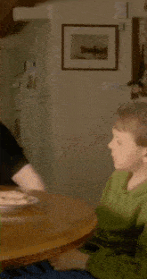 a boy in a green shirt is sitting at a table with other people