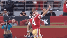 a football player wearing a red jersey with the number 4 on it is pointing up at the crowd .