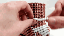 a person is playing with a stack of copper beads and white beads