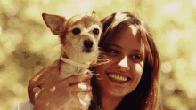 a woman is holding a small dog in her arms and smiling at the camera .