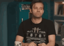 a man is sitting at a table holding a cup of coffee and looking down .
