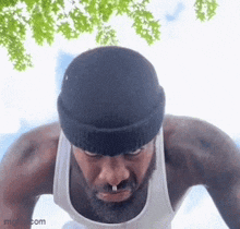a man with a beard wearing a black beanie and a white tank top is doing push ups .
