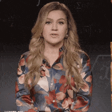 a woman wearing a floral shirt stands in front of a mathematical background