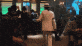 a man in a white suit and hat is dancing in a club