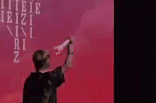 a man in a black shirt is standing in front of a red wall and holding a microphone .