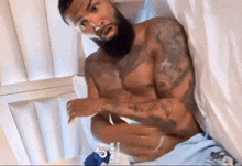 a shirtless man with a beard is laying in bed .