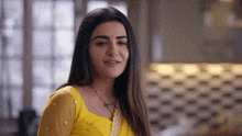 a woman wearing a yellow top and a black necklace smiles
