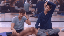 two men sit on yoga mats in front of a mirror