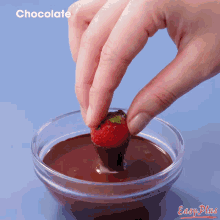 a person dipping a strawberry in a bowl of chocolate sauce