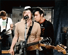 a man is singing into a microphone while another man plays guitar .