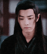a young man with long hair is wearing a black top