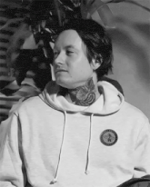 a black and white photo of a man with a tattoo on his neck wearing a white hoodie .