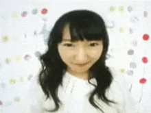 a woman in a white shirt is smiling in front of a white background with flowers .