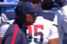 a man wearing headphones stands in front of a football player wearing a jersey with the number 15 on it