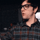 a man wearing glasses and a plaid shirt stands in front of a red sign that says ress