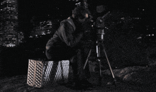 a man is looking through a telescope while sitting on a box