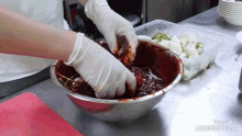 a person wearing gloves is mixing food in a metal bowl with the words made in animatica on the bottom
