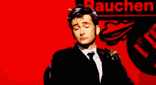 a man in a suit and tie with his eyes closed in front of a sign that says rauchen