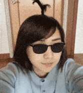 a woman wearing sunglasses takes a selfie with her hair in a bun
