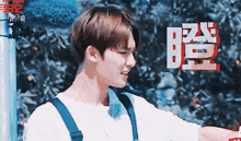 a young man wearing a white shirt and blue overalls stands in front of a sign that says ' korean '