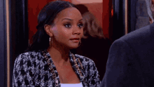 a woman wearing hoop earrings and a black and white jacket looks surprised