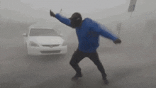 a man in a blue jacket is standing in front of a white car in the fog .