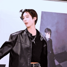 a young man wearing a black leather jacket is standing in front of a wall .