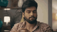a man with a beard wearing a plaid shirt is sitting with his eyes closed