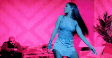a woman in a blue dress is dancing in a living room with a man sitting on a couch .