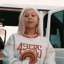 a woman wearing a 49ers sweater is standing in front of a white van .