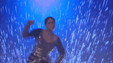 a woman is dancing in the rain on a stage in front of a blue light .