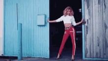 a woman in a white crop top and red pants is standing in front of a blue wall .