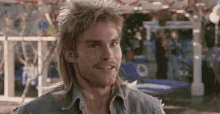 a man with a mullet and a denim shirt is smiling in a park .