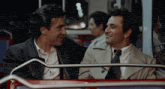 two men are sitting on a bus and looking at each other