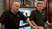 two men in black shirts are standing next to each other in front of a display case