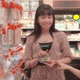 a woman wearing a ganni shirt is holding a green object in her hand