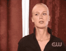a woman is standing in front of a red curtain with the letters cw on her shirt